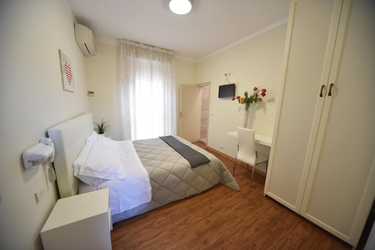 A bedroom with a bed, a desk, a chair, a TV, and a wardrobe.