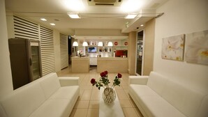 A hotel lobby with white sofas, a reception desk, a kitchen area, and a vase with flowers. - Villa Edda (Riccione)