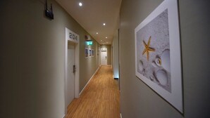 A hallway with wooden flooring, numbered doors, and a framed picture of seashells and starfish on the wall. - Villa Edda (Riccione)