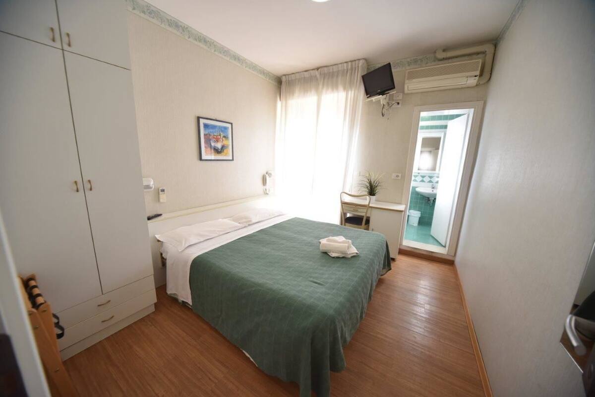 A hotel room with a bed, a desk, a chair, a television, and a bathroom visible through an open door.
