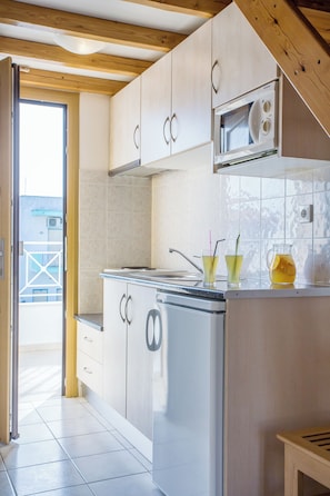 A kitchen with a microwave, cabinets, and a sink. There is a door leading outside.