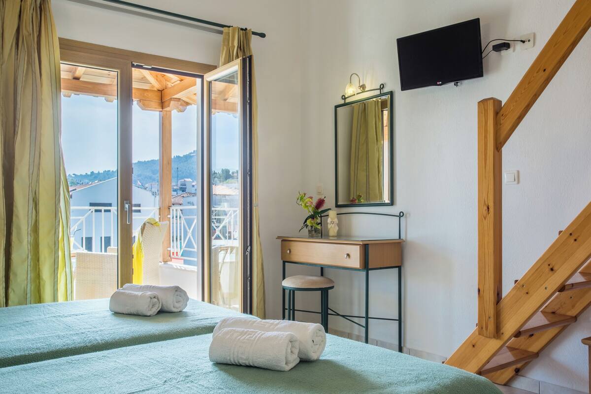 Una habitación con una cama, un escritorio de madera, un espejo, un televisor y una escalera.