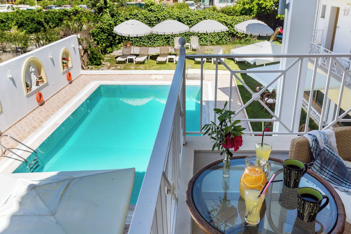 Zona junto a la piscina con mesa de vidrio, sillones reclinables y sombrillas.