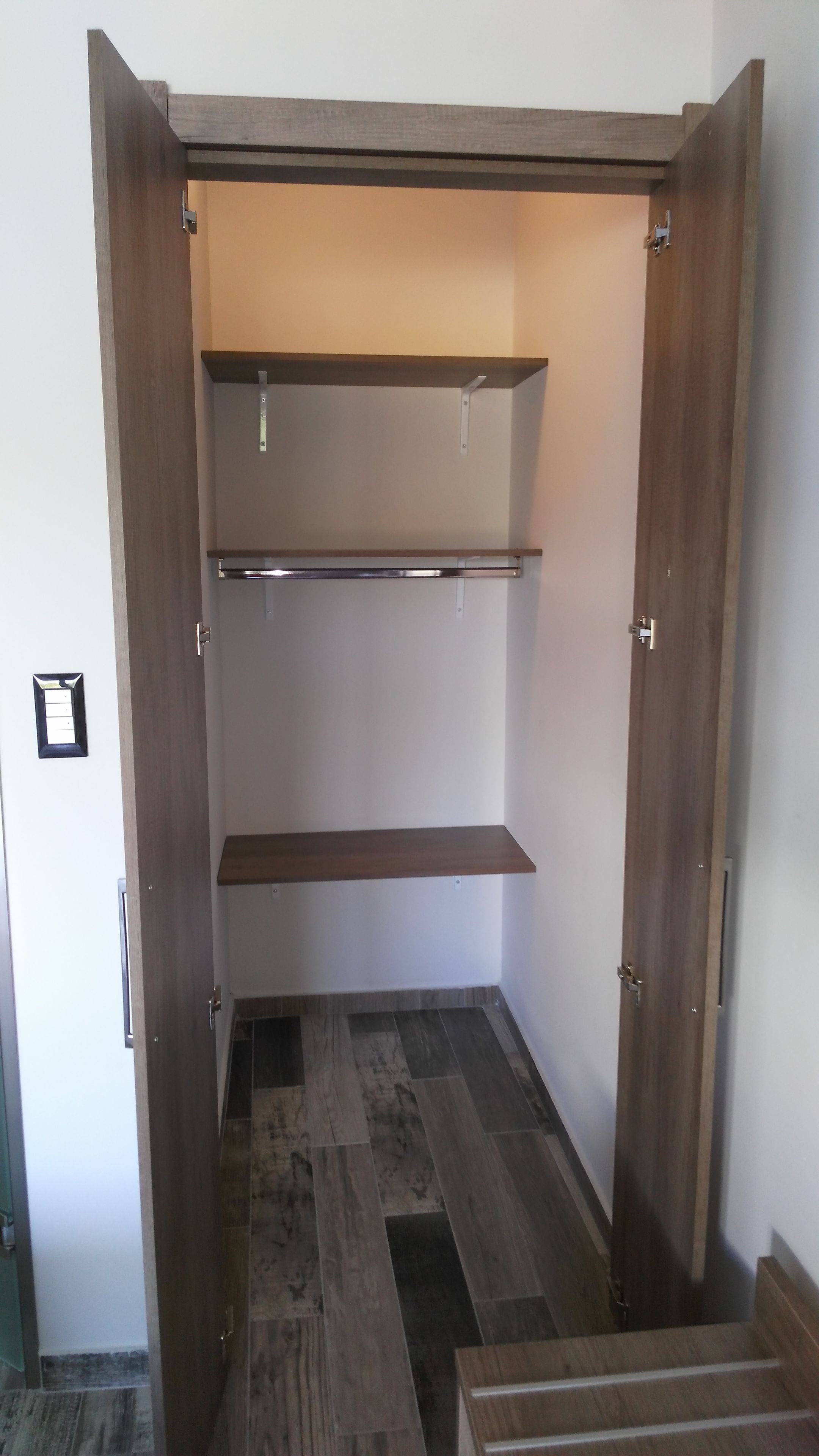 Un dressing avec des portes en bois, deux étagères et un sol carrelé.