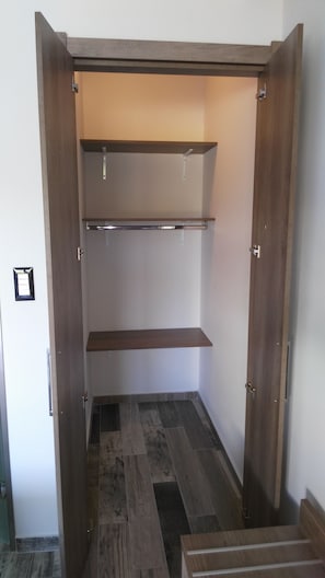 A walk-in closet with wooden doors, two shelves, and a tiled floor.