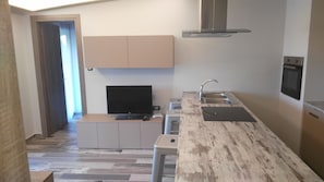 A modern kitchen with a built-in oven, a stainless steel sink, and a flat-screen TV. - Bright Star (Rhodes)