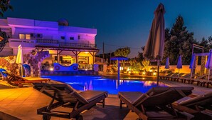 A pool area with lounge chairs and umbrellas, a building with a balcony, and a bar area. - Bright Star (Rhodes)