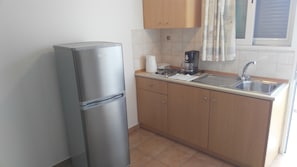 A compact kitchen with a refrigerator, a coffee maker, a sink, and wooden cabinets.