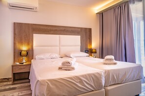 Habitación de hotel con dos camas, cabecera de madera, lámparas de noche, mesitas de noche y una ventana con cortinas.