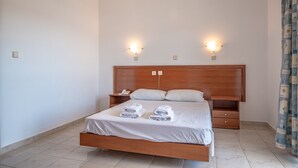 A neatly made bed with white linens and two towels, a wooden headboard, bedside tables with lamps, and a patterned curtain. - Bright Star (Rhodes)