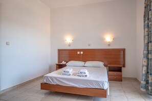 A neatly made bed with white linens and two towels, a wooden headboard, bedside tables with lamps, and a patterned curtain. - Bright Star (Rhodes)