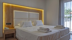 A modern hotel room with a large bed, a bedside table with a phone, and a view of the outdoors through large windows. - Bright Star (Rhodes)