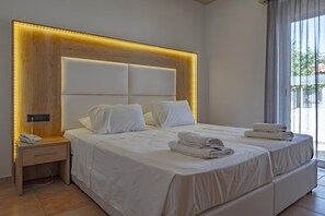 A modern hotel room with a large bed, a bedside table with a phone, and a view of the outdoors through large windows. - Bright Star (Rhodes)