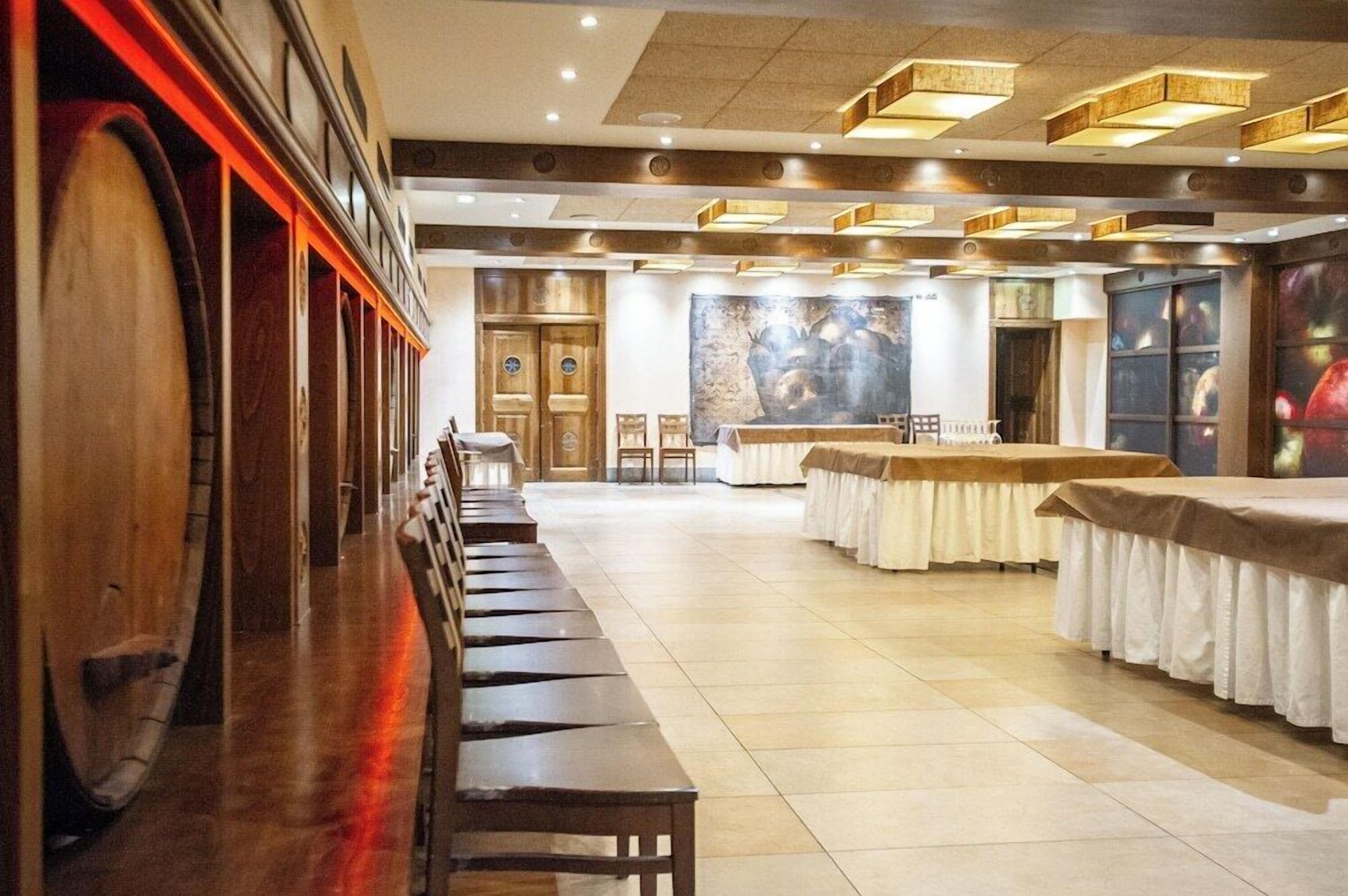 Une vaste salle de banquet dotée de longues bancs et tables en bois, d’un éclairage encastré et d’une grande fresque murale au fond.
