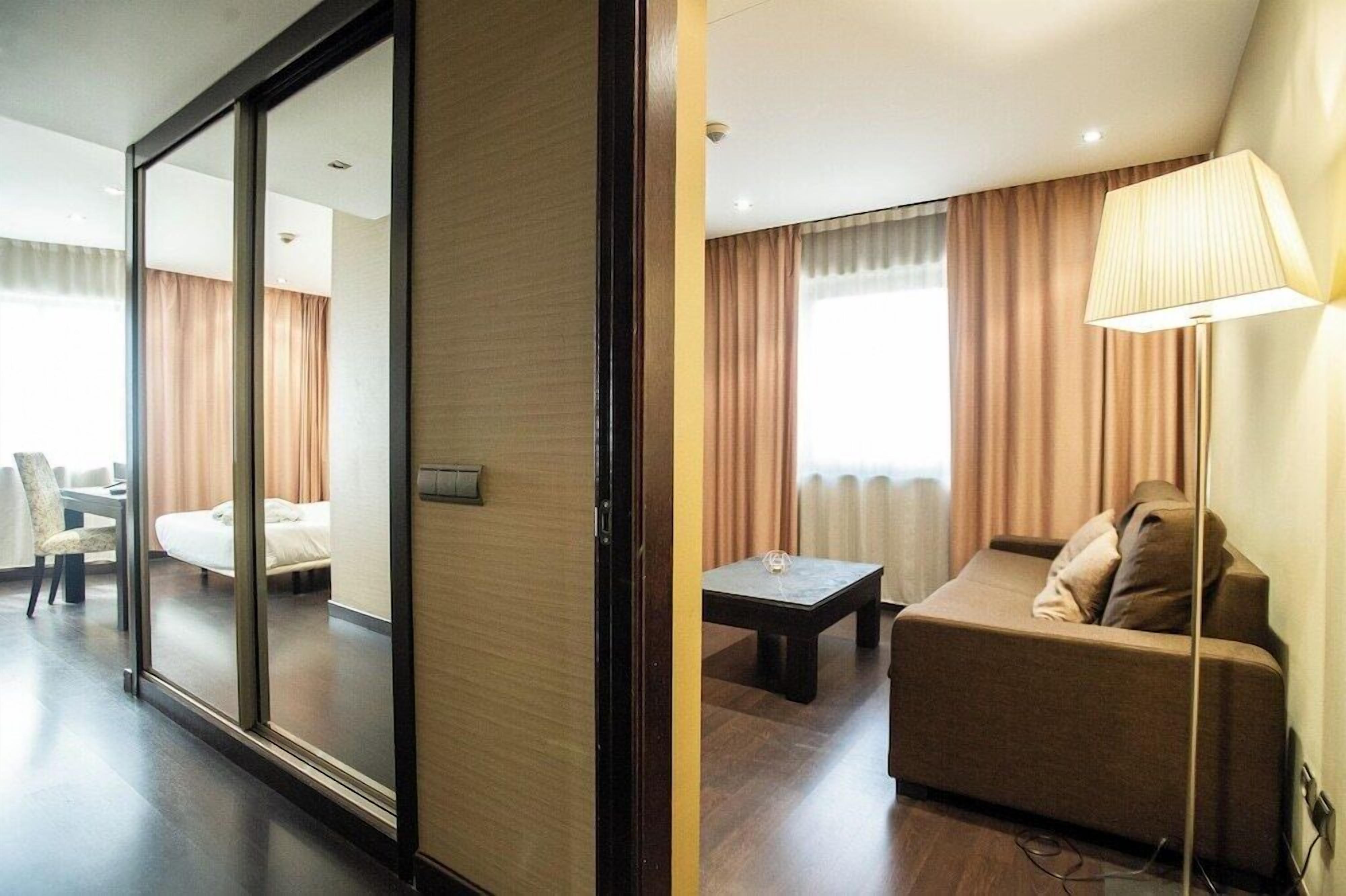 Habitación de hotel con puerta corrediza que da a un balcón, un sofá, una mesita y una lámpara.