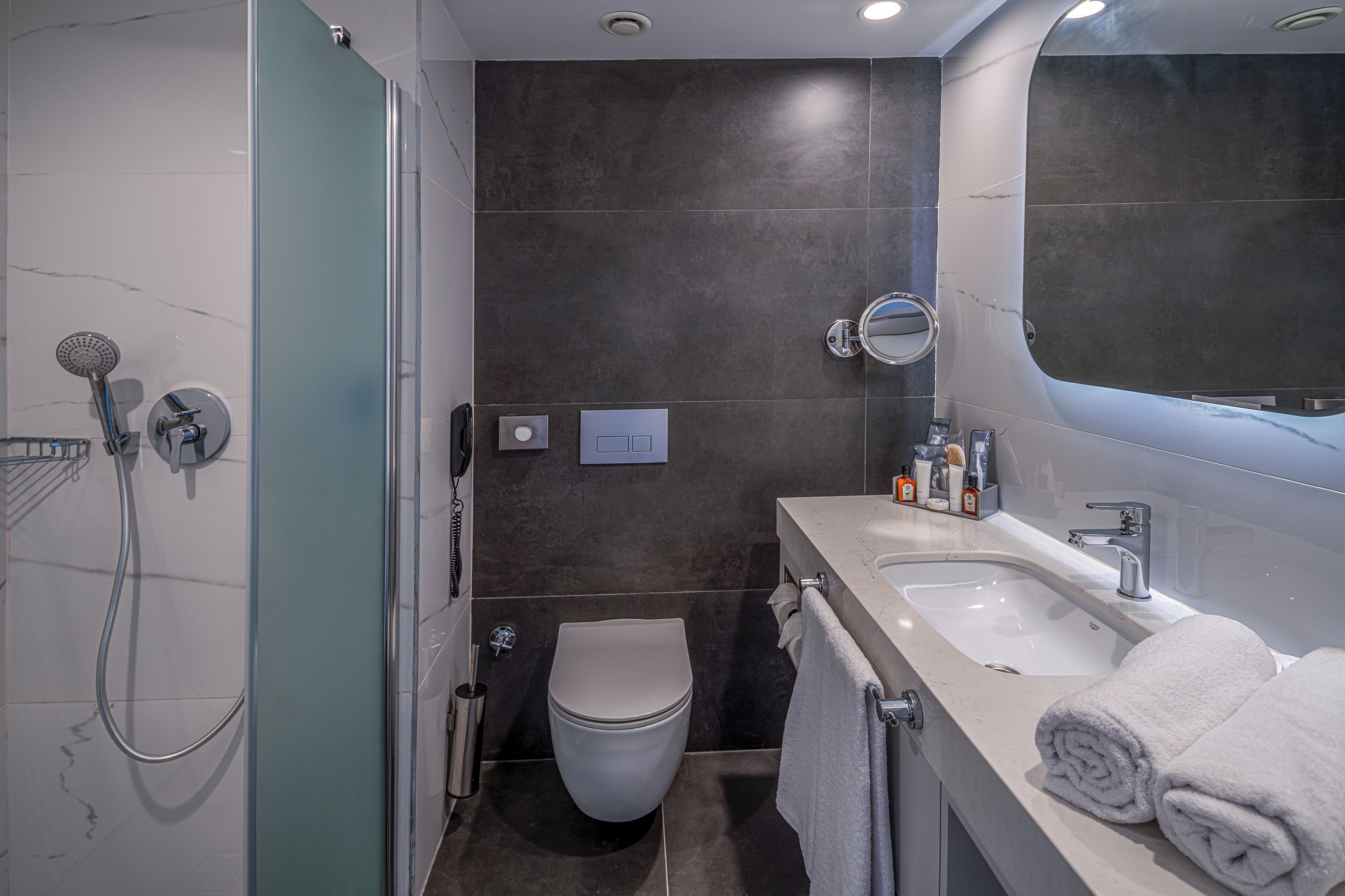 A modern bathroom with a glass shower enclosure, a toilet, a sink with a mirror, and neatly folded towels.