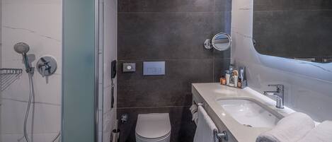 A modern bathroom with a glass shower enclosure, a toilet, a sink with a mirror, and neatly folded towels.