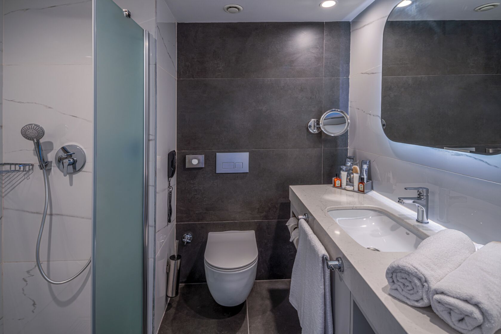 Een moderne badkamer met een douchecabine van glas, een toilet en een wastafel met een wasbak en spiegel.