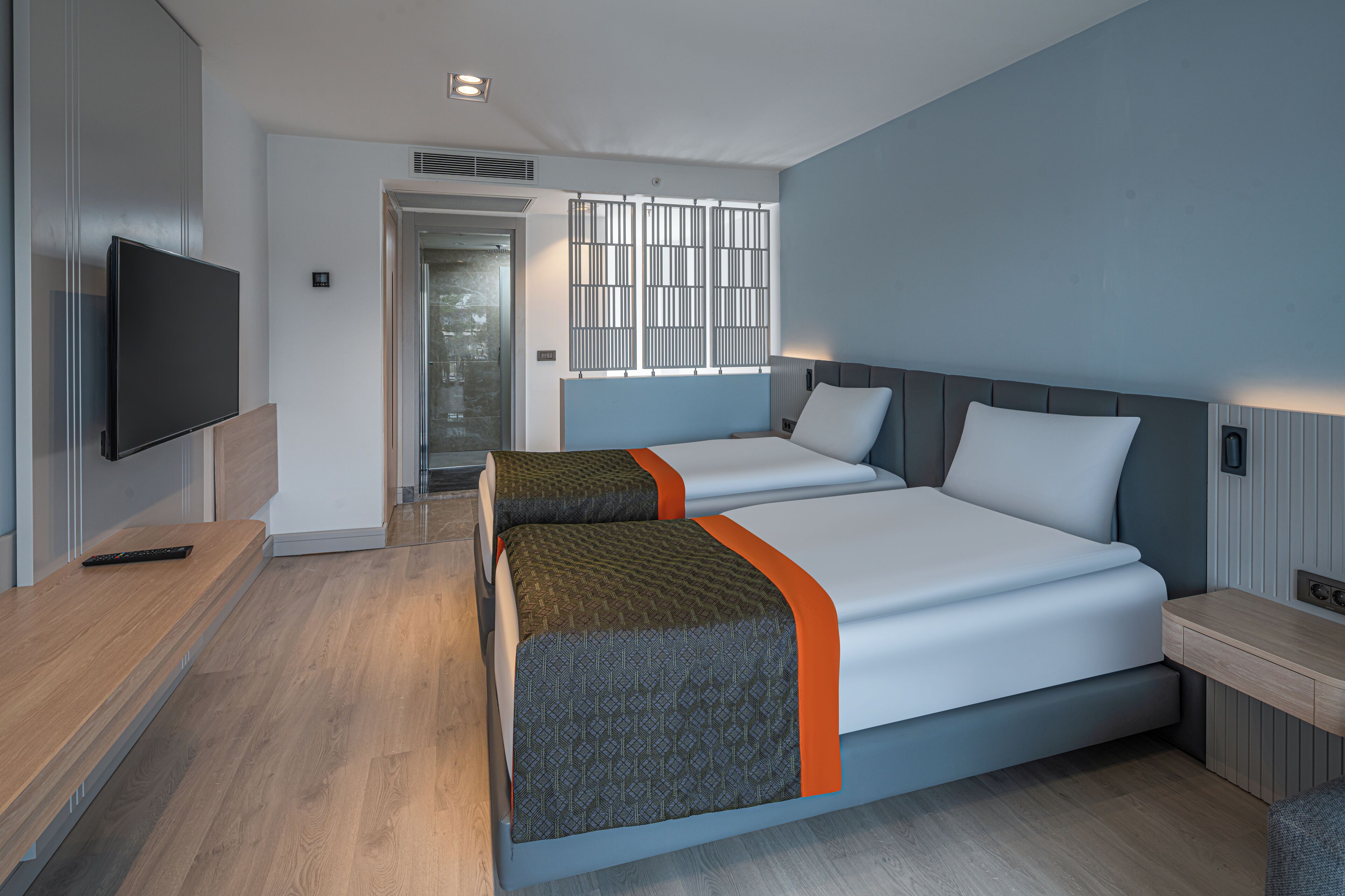 A modern hotel room with two beds, a TV, and a wooden desk.
