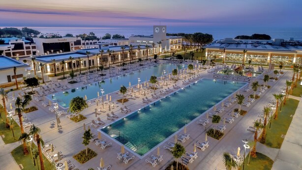 Ein Resort mit großem Schwimmbad, Liegestühlen und einem Uhrturm.