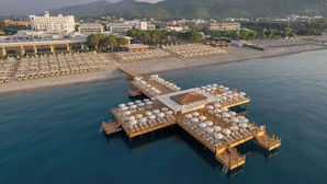 Vista aérea de un resort costero con múltiples plataformas flotantes conectadas por pasarelas, con filas de tumbonas y sombrillas.