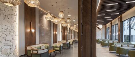 A modern hotel lobby with tiered seating, pendant lighting, and a stone accent wall.