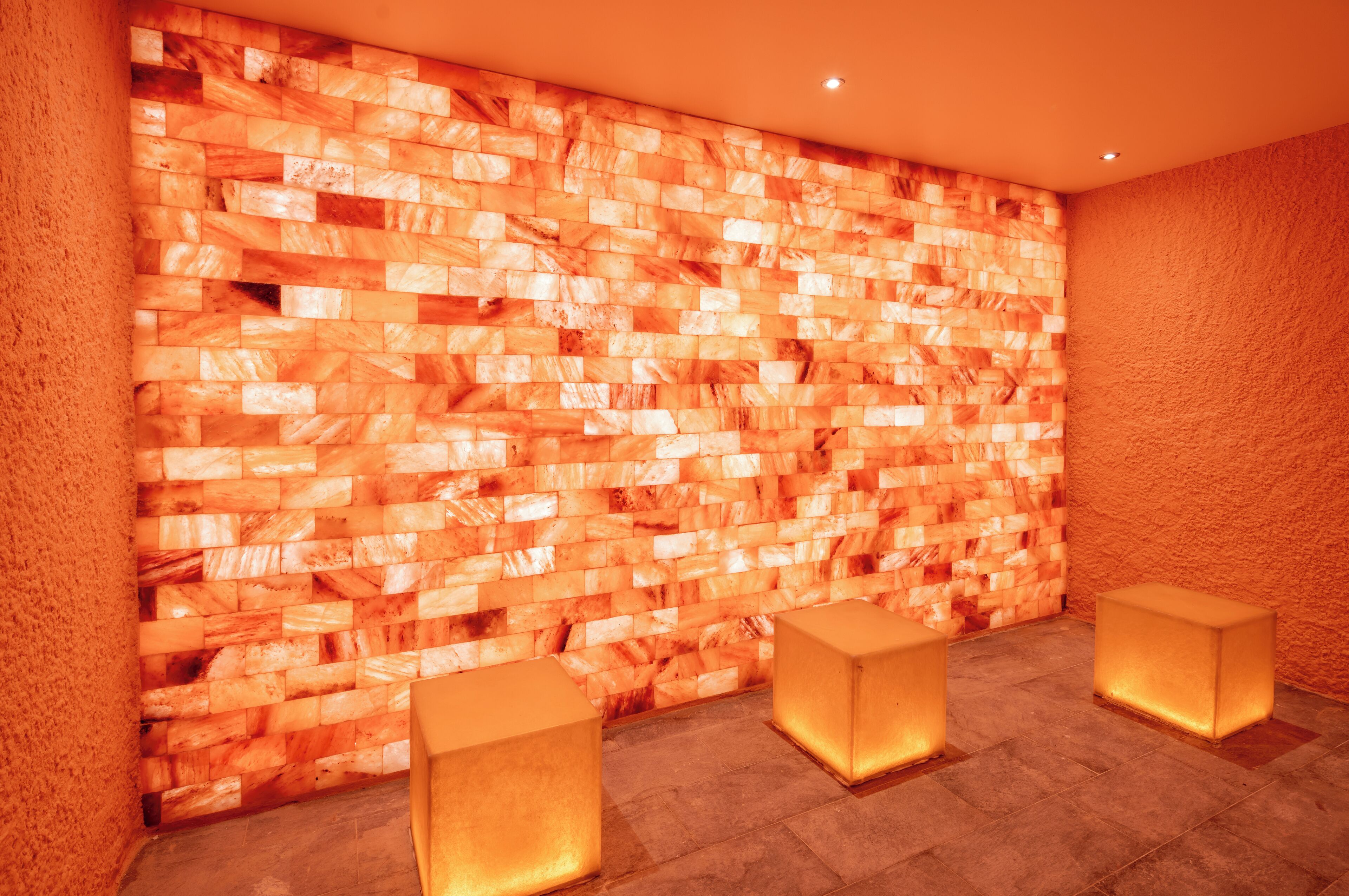 A wall with a textured pattern, three illuminated square stools, and a ceiling light.