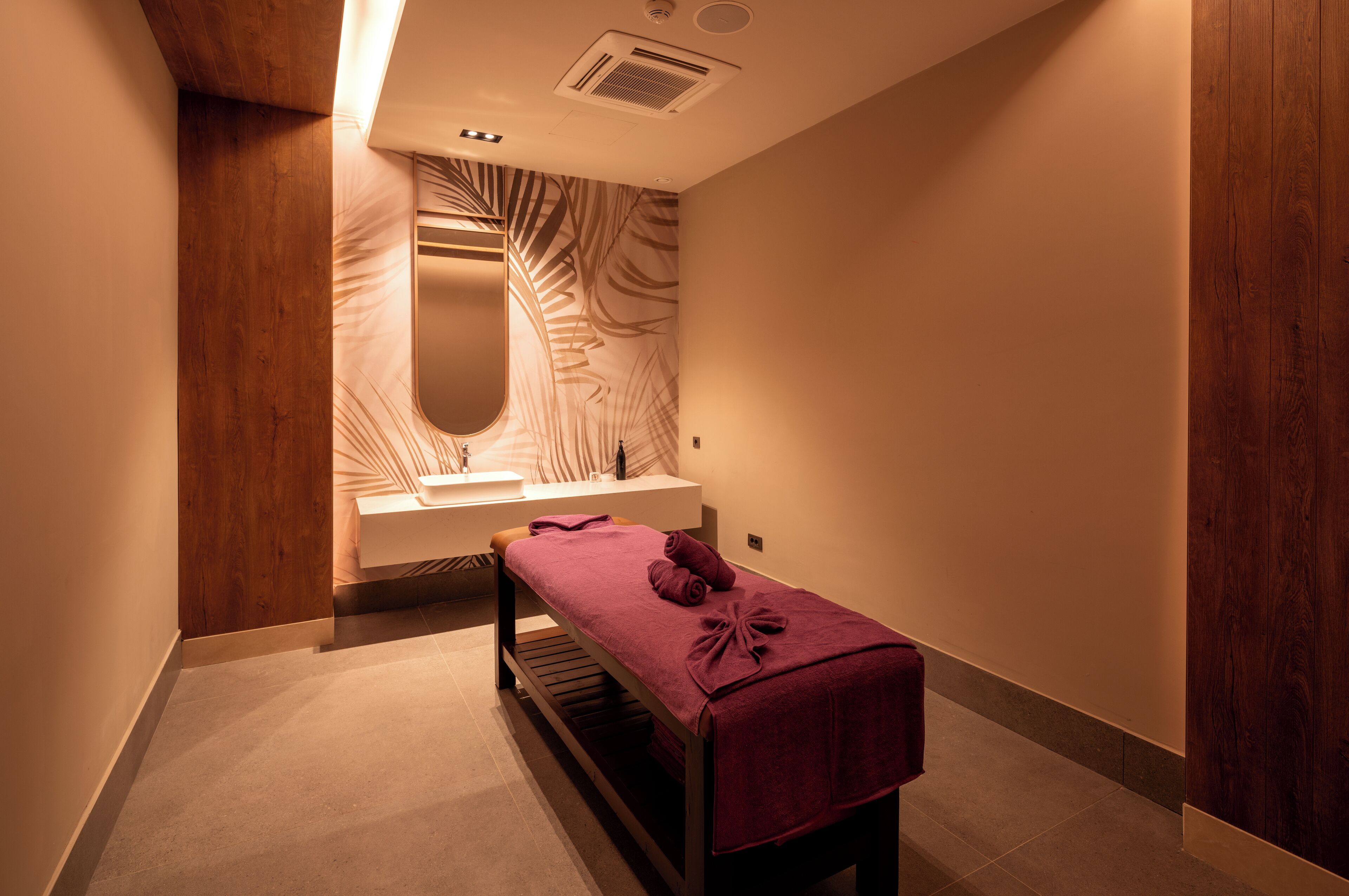 Un cuarto de spa con un banco de madera, un lavamanos y un espejo con un diseño de hojas.