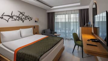 Habitación de hotel con cama, escritorio con silla, televisión y balcón con vistas.