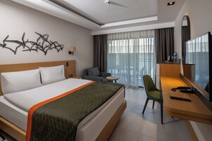 Habitación de hotel con cama, escritorio con silla, televisión y balcón con vistas.
