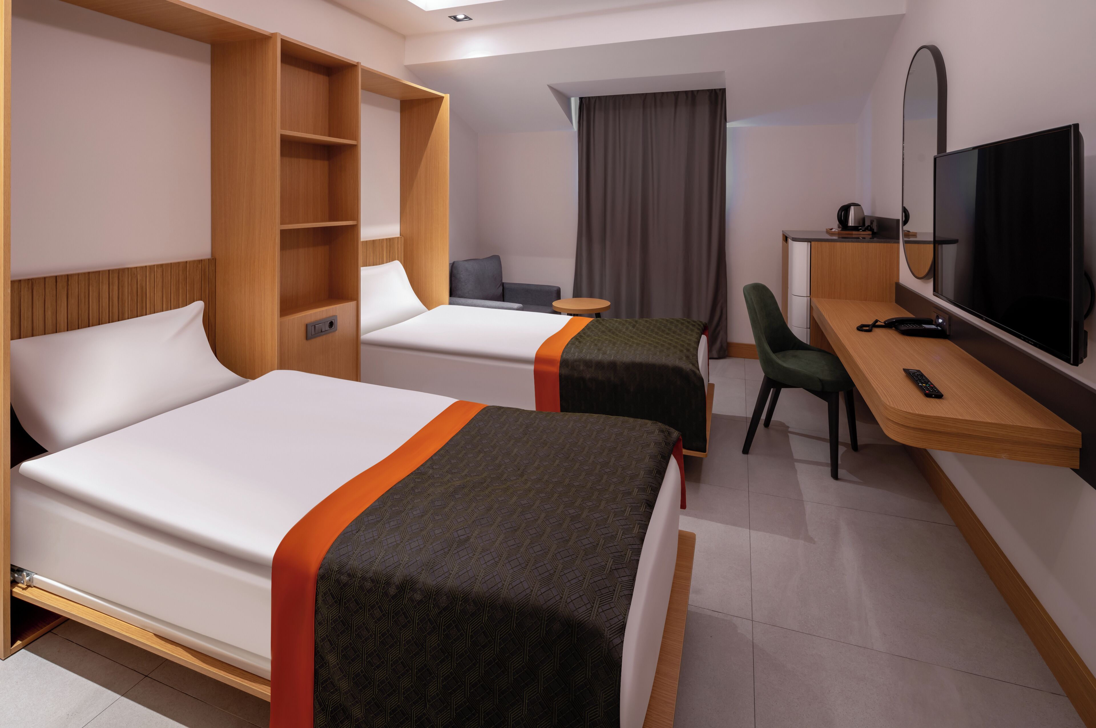 Ein Hotelzimmer mit zwei Betten, einem Schreibtisch mit Fernseher, einem Sessel, einem kleinen Tisch und einem Kleiderschrank.