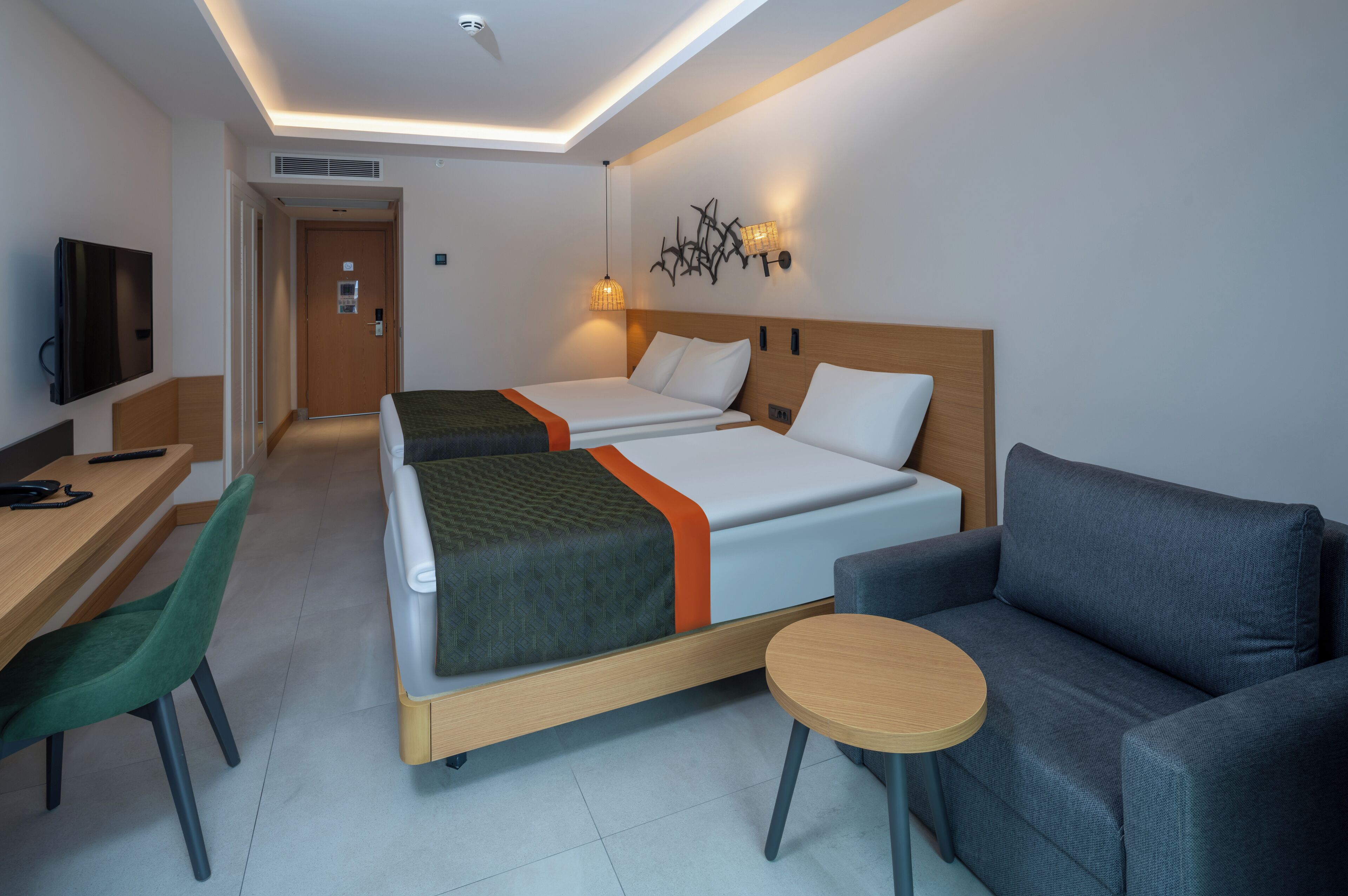 A hotel room with a bed, a desk, a chair, a sofa, and a small table.