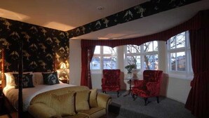 A hotel room with a bed, a sofa, two armchairs, a table, and a window with curtains. - The Max Brighton (Brighton)