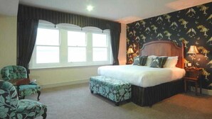 A hotel room with a large bed, a chair, a nightstand, and a window with curtains. - The Max Brighton (Brighton)