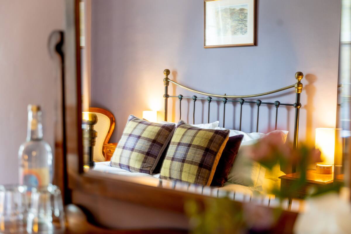 A neatly made bed with plaid pillows, a bedside table with a lamp, and a framed picture on the wall.