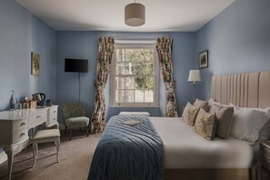 A bedroom with a bed, a desk, a chair, a television, and a window with curtains.