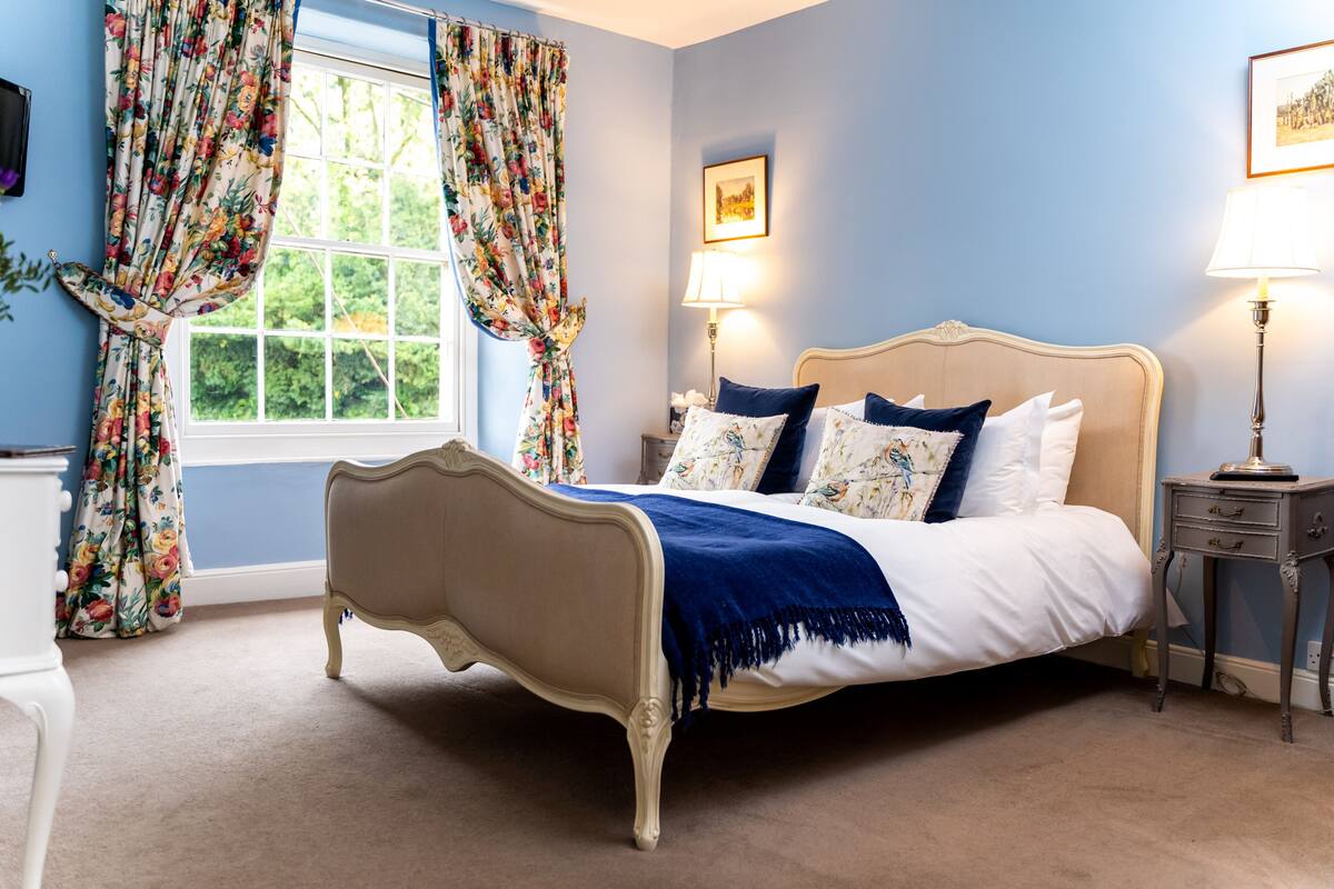 A bedroom with a bed, curtains, a bedside table, and a lamp.
