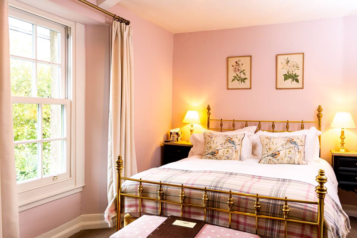A bedroom with a bed, two bedside tables, a window with curtains, and two wall-mounted lamps.