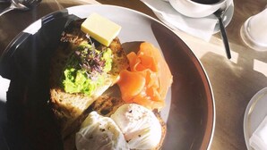 A breakfast plate with toast, avocado, and eggs, a glass of orange juice, and a cup of coffee on a table.