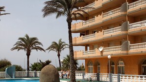 Zona d'una piscina d'hotel amb una gran roca com a element central, palmeres i un edifici d'àmples balcons.