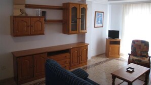 Un saló amb un sofà, armaris de fusta, una televisió i una cadira estampada.