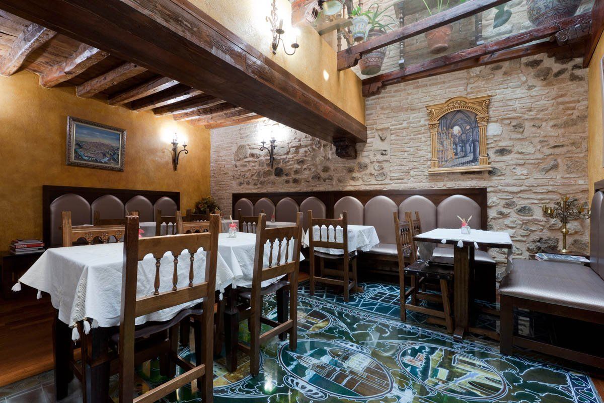 Un restaurante con mesas y sillas de madera, paredes de piedra y piso de baldosas.