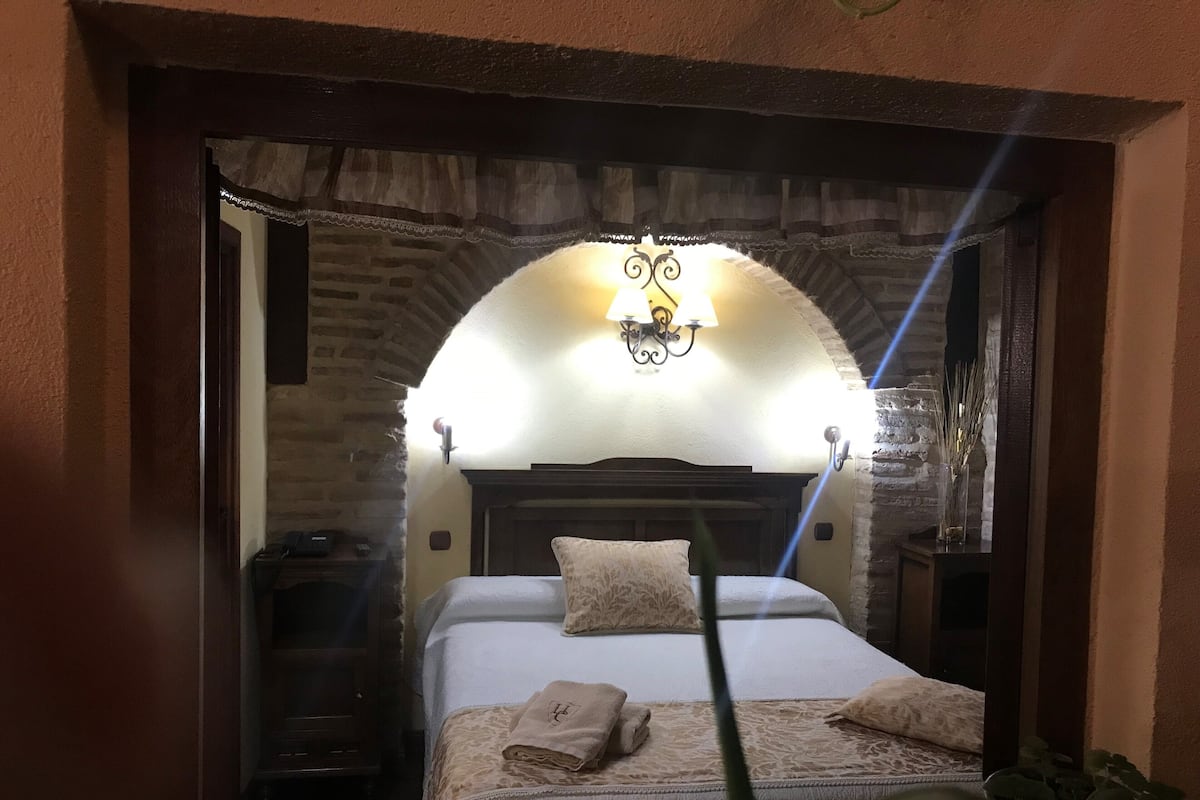 Quarto com cama, almofadas, mesa de cabeceira e abajur.