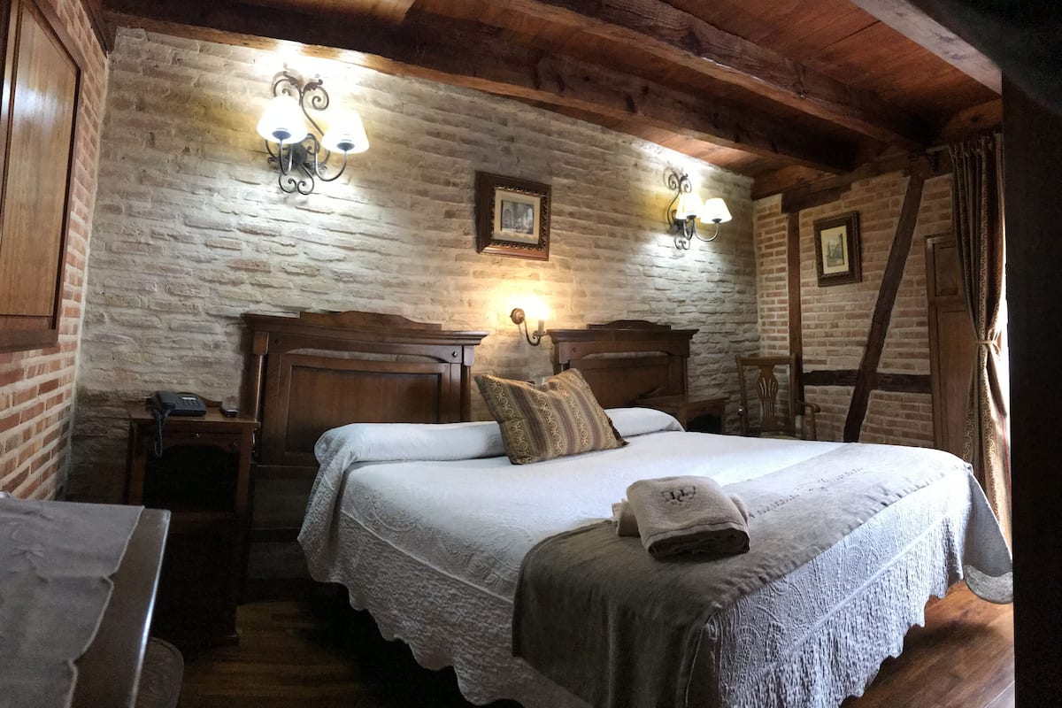 Um quarto aconchegante com uma cama de madeira, duas mesas de cabeceira, um telefone e uma parede de tijolos.