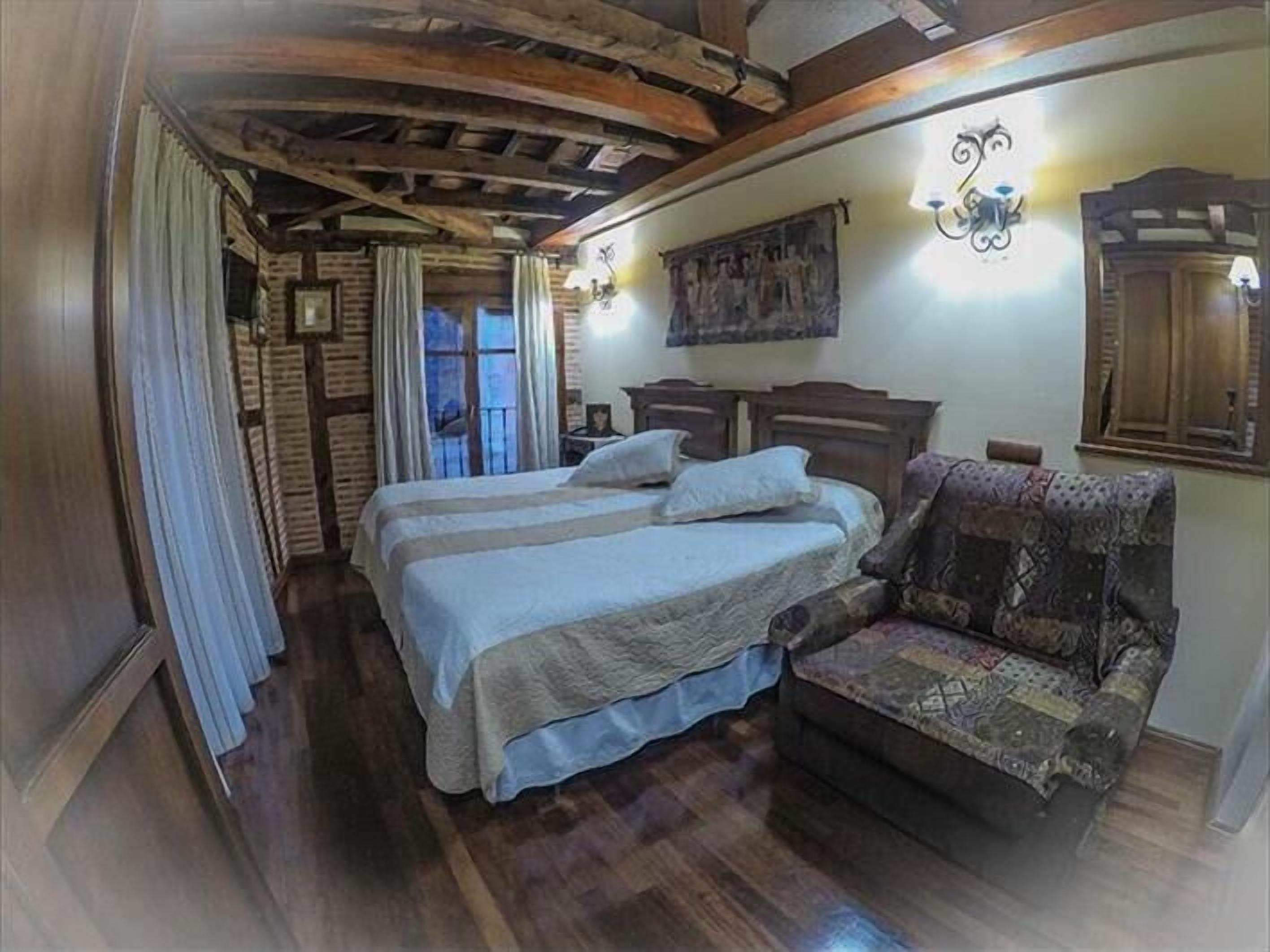 A bedroom with a bed, a chair, wooden beams on the ceiling, and a window with curtains.