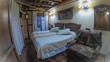 A bedroom with a bed, a chair, wooden beams on the ceiling, and a window with curtains.