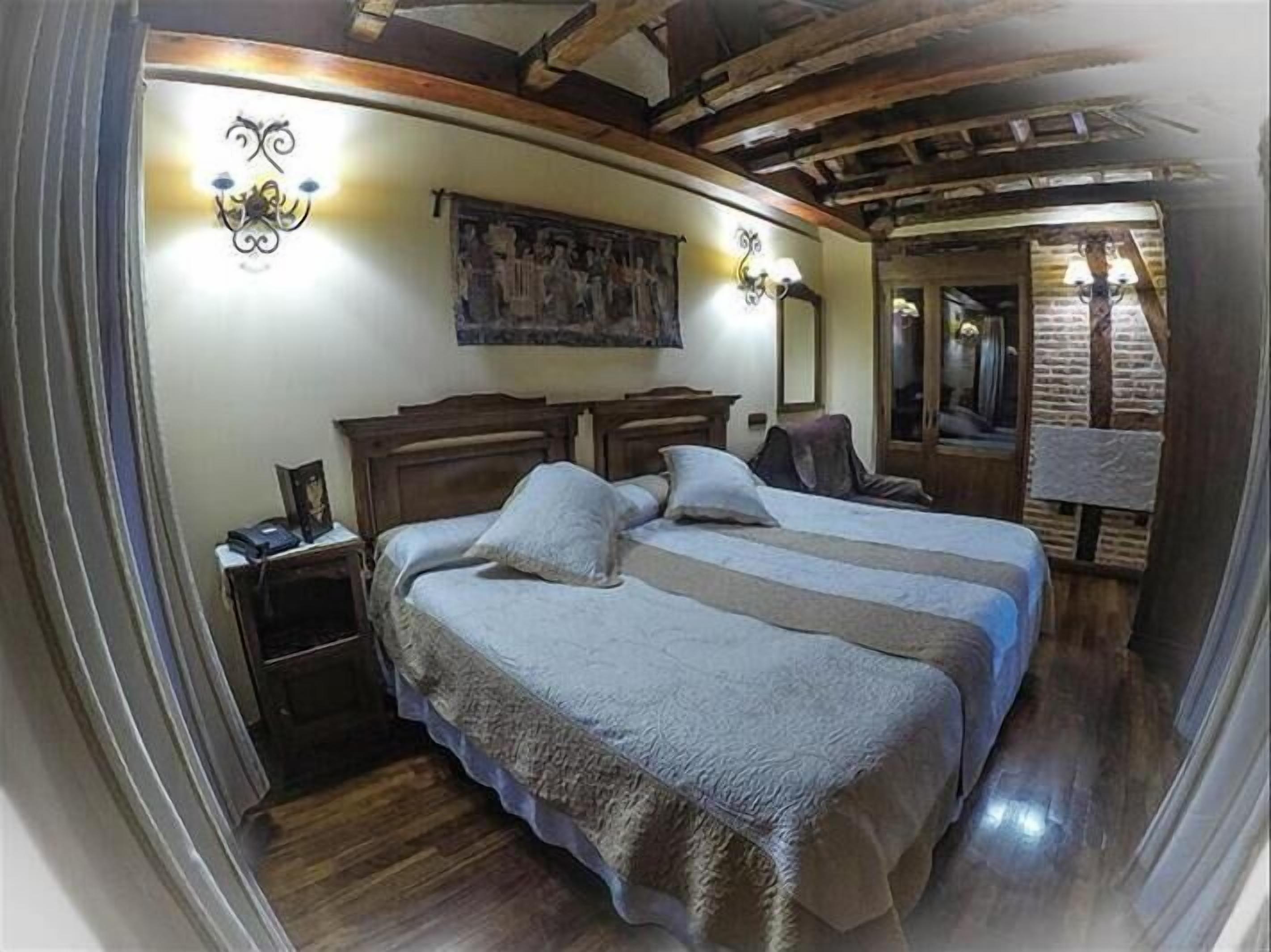 A bedroom with a wooden bed, a nightstand, a wall-mounted lamp, and a mirror.