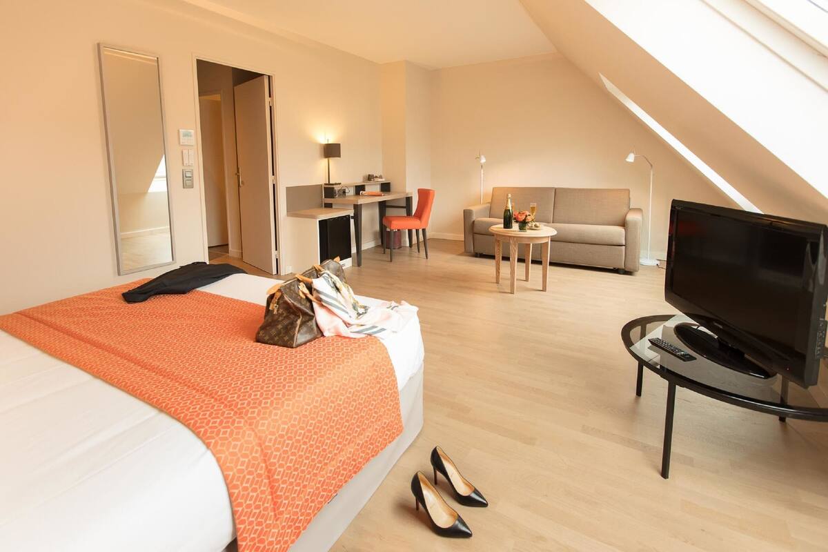 A hotel room with a bed, a desk, a sofa, a TV, and a small table.