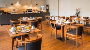 A hotel dining area with multiple wooden tables and chairs, breakfast items, and a coffee station. - Hôtel Montbriand Antony (Antony)