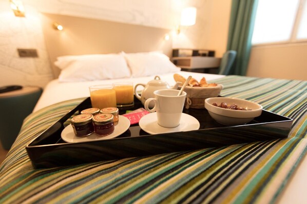 Una bandeja de desayuno ordenada sobre una cama con cubrecama a rayas, que incluye una taza, jugo, frascos de mermelada y pan.